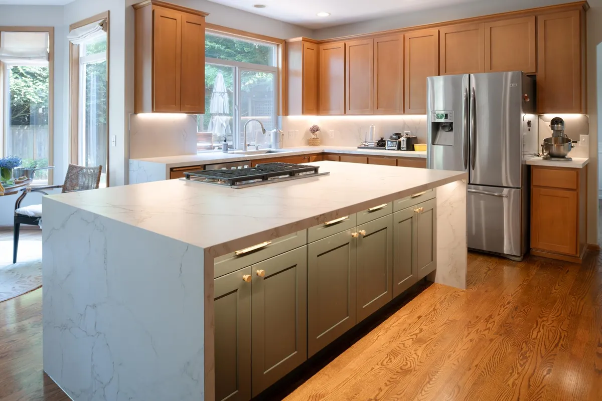 Kitchen with a sage green island, marble-look waterfall counters and maple cabinets