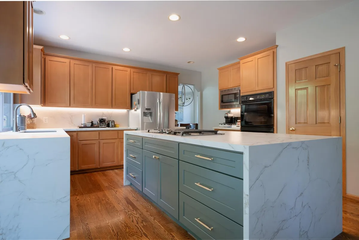 Sage green island with a marble-look waterfall edge and brass pulls