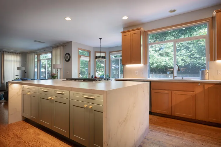 Sage island and maple cabinets in an open kitchen with garden windows