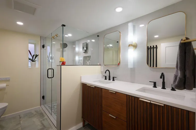 Walnut vanity and a glass shower in a white bathroom
