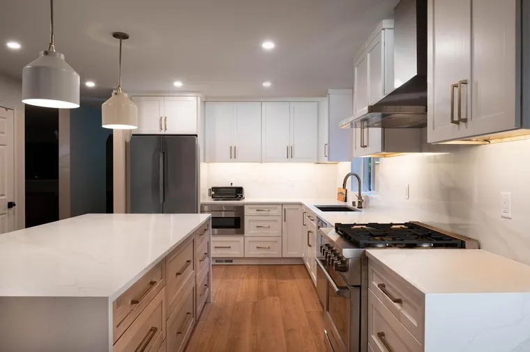 White kitchen with a wood island base, white pendants and a stainless hood