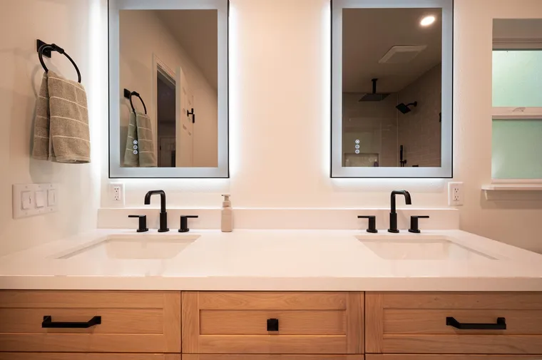 Double vanity with lit mirrors and black faucets