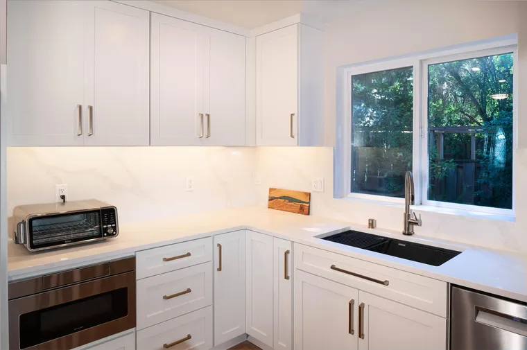White kitchen corner with a marble-look slab backsplash and a brass faucet