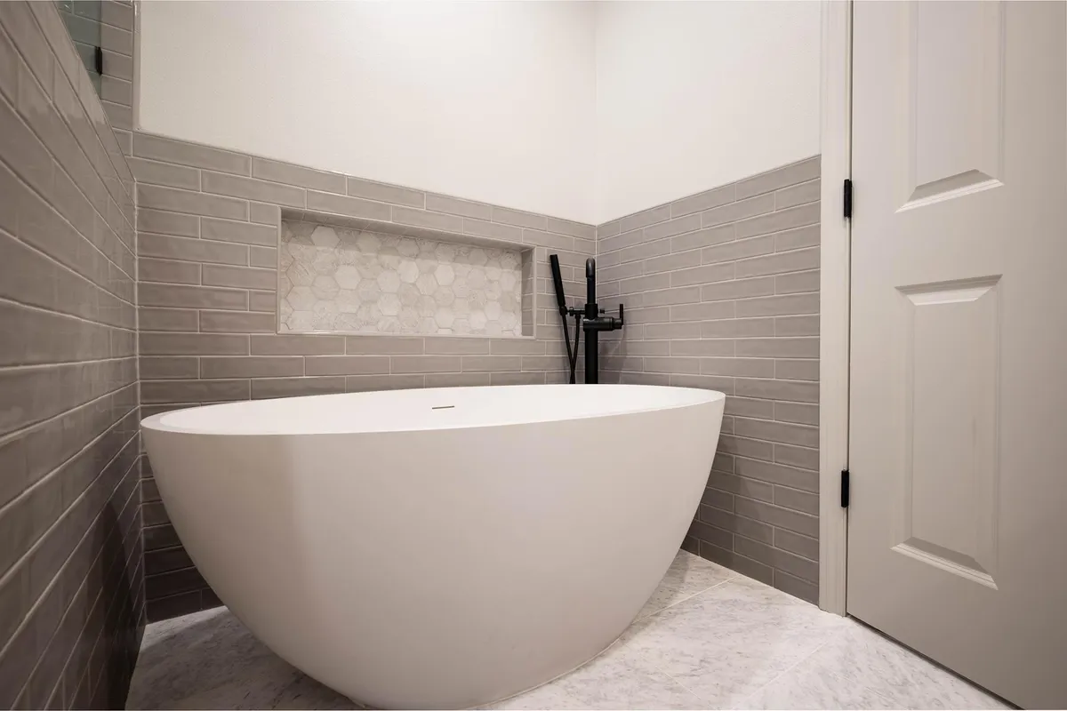 Freestanding tub in front of gray tile with a long niche