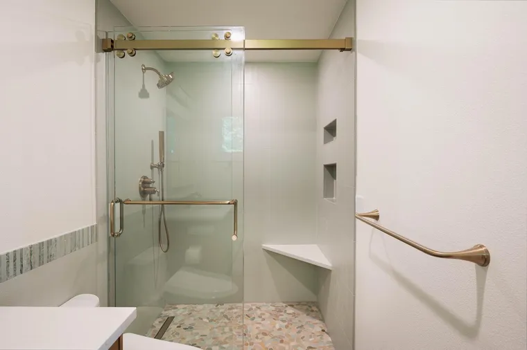 Glass shower with brass fixtures and a pebble floor