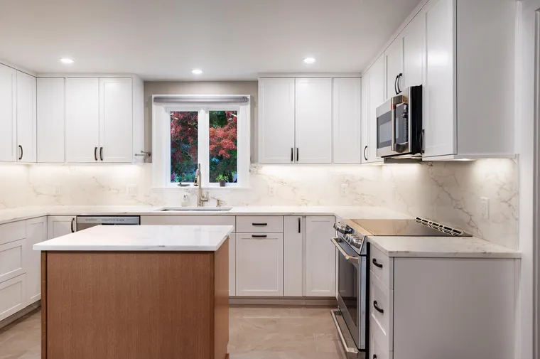 White shaker kitchen with a wood island and a marble-look backsplash