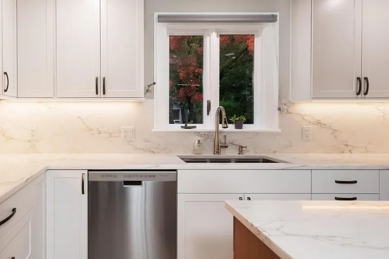 Sink under a garden window with white shaker cabinets and a dishwasher