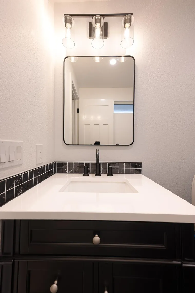 Black vanity with a white top and a black hex tile backsplash