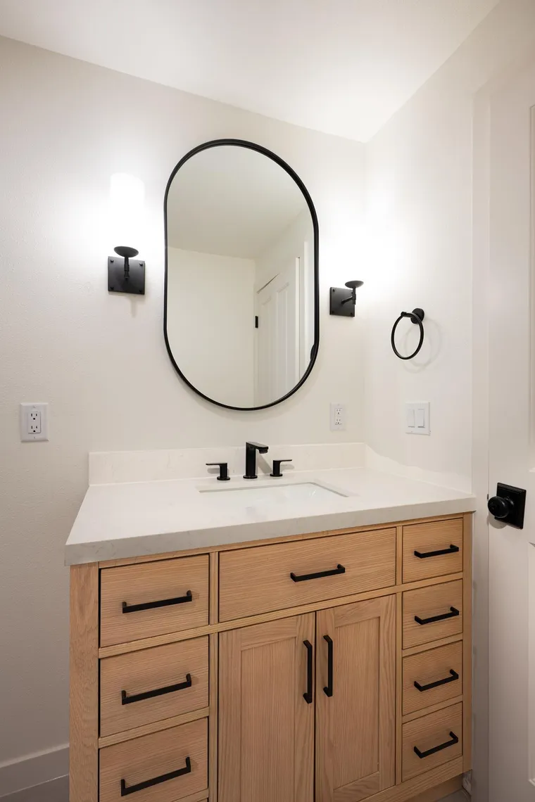 Oak vanity with an oval black mirror and matching sconces