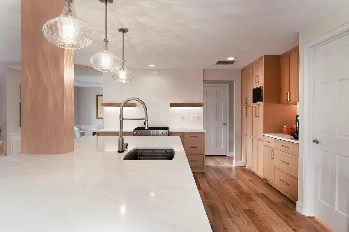 Long white island with a sink and glass pendants over a wood floor
