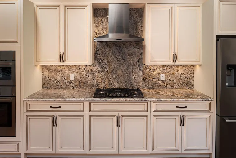 Cream raised-panel cabinets with a granite backsplash and a chimney hood