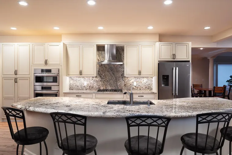 Curved granite island with bar stools and cream cabinetry