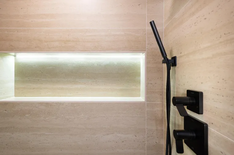 Lit shower niche in travertine-look tile with a black handheld shower