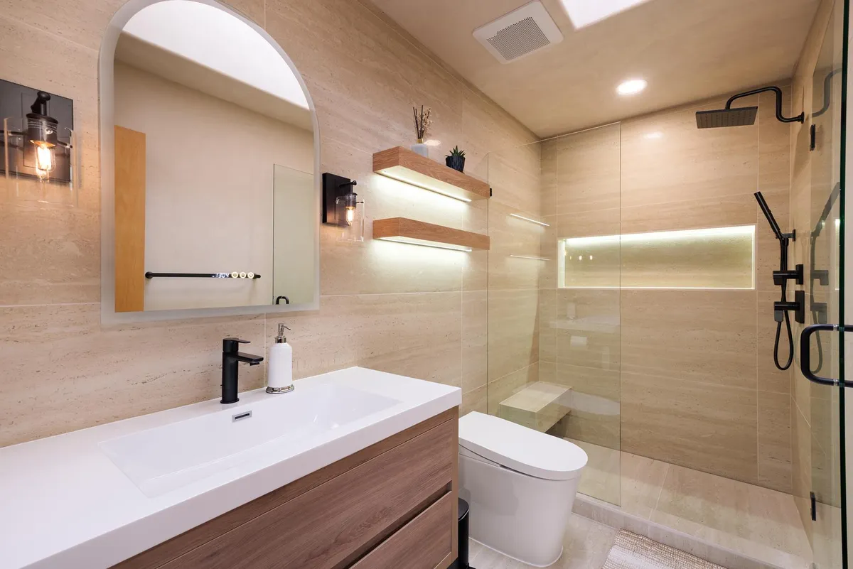Travertine-look bathroom with an arched mirror, floating shelves and a glass shower