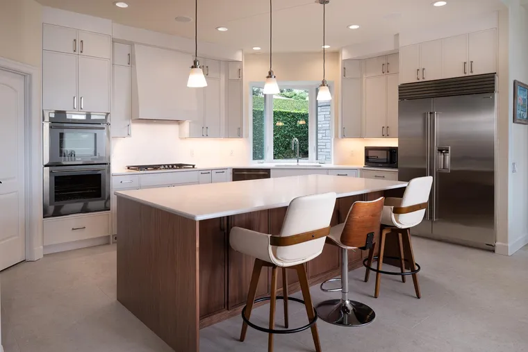 White kitchen with a walnut island, counter stools and pendant lights