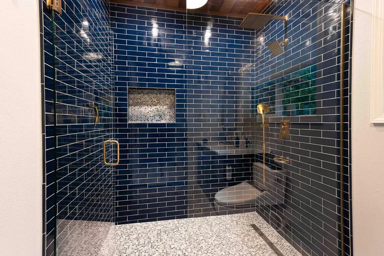 Walk-in shower in navy glazed tile with brass fixtures and a terrazzo-look floor