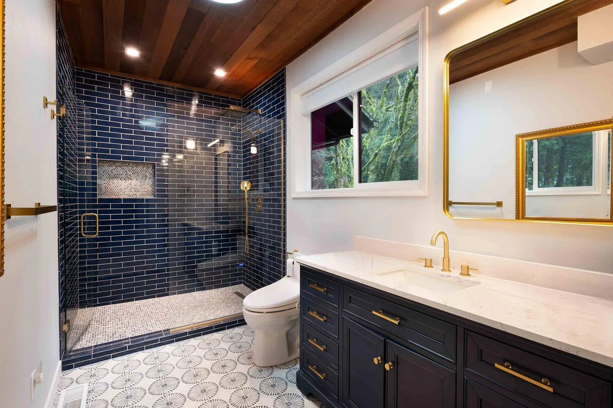 Navy vanity, brass mirrors and a blue tiled shower under a cedar ceiling