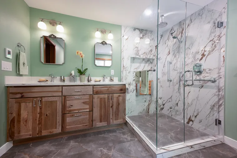 Sage green bathroom with a wood vanity and a marble-look glass shower