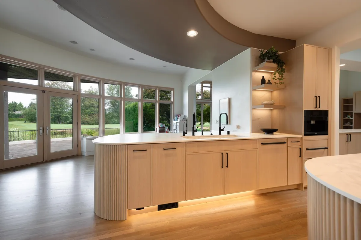 Curved island with a fluted white oak base facing a wall of windows